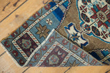 Folded corner of a distressed Oushak rug, showing low pile, blue, aubergine, and ivory border.