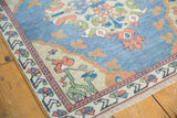 Corner of vintage distressed Oushak rug: beige spandrel, green vines, terracotta buds, low pile.