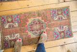 Distressed Oushak rug showing low pile texture with blush and fuchsia plant motifs.