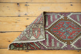 Folded corner of distressed Oushak runner with aubergine, green, red geometric patterns.
