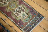 Distressed Oushak runner's colorful geometric border patterns and white fringe.