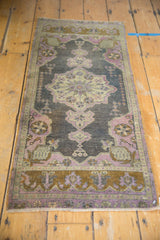 Distressed Oushak mat corner, mauve and aubergine florals, bronze border, worn pile.