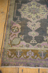 Distressed vintage Oushak rug corner displaying pale aubergine pinwheel motifs and time-softened pile.