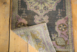 Distressed Oushak rug corner revealing faded dark pile, mauve patterns, and reverse foundation.