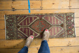 Distressed vintage Oushak runner's serrated aubergine and rust medallion, showing worn pile.