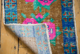 Distressed Oushak rug, showing bright pink floral design, worn pile, and hand-knotted foundation.