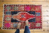 Distressed Oushak rug top corner with bright fuchsia, celadon green, and navy floral motifs.