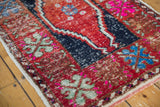 Distressed red Oushak rug close-up showing celadon floral, bright fuchsia, and stepped navy details.