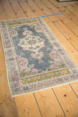 Distressed Oushak rug corner showing floral pinwheel motif in pale purple, ivory, and bronze.