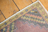Distressed vintage Oushak rug corner showing worn dusty mauve pile and checker border.