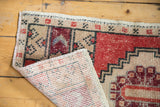 Distressed vintage Oushak rug corner showing worn red and beige pile, plus hand-knotted foundation.