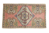Vintage distressed Oushak rug with pale rose field, stepped silver medallion, green motifs.