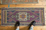 Distressed Oushak rug corner: stepped plant motif, geometric borders, purple, navy, gold.