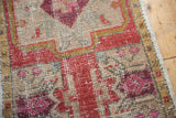 Distressed vintage Oushak rug corner with beige field, raspberry seedling motif, and prominent wear.