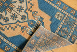 Folded corner of vintage Oushak rug reveals distressed pile, fringe, and hand-knotted reverse.