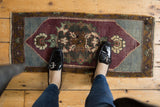 Vintage Oushak mat with distressed aubergine, slate blue, and bronze tones, showing an ornate medallion.