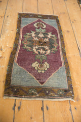 Distressed Oushak rug corner featuring aubergine field, slate blue spandrel, and ivory palmette.