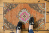 Distressed Oushak rug's central Rococo-inspired medallion with fuchsia and dusty orange.