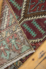 Distressed vintage Oushak rug corner revealing textured aubergine pile, faint foundation, and fringe.