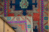 Distressed Oushak rug corner showcasing geometric patterns, bright fuchsia, blue, and secured side.