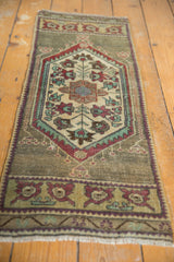 Distressed vintage Oushak rug close-up: geometric patterns, ivory, green, wine red, visible wear.