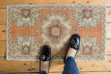 Upper corner of distressed Oushak mat, featuring pale tangerine, antique ivory, and faded wine red Rococo motifs.