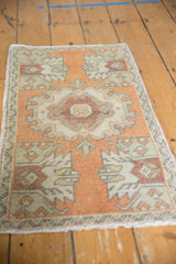 Distressed Oushak rug mat texture: tangerine, faded wine, and ivory geometric patterns with intact selvage.