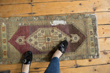 Distressed vintage Oushak runner with geometric starburst medallion, aubergine field, and exposed foundation.