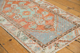 Distressed Oushak rug runner showcasing brick red and mint green floral motifs and serrated border.