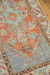 Distressed vintage Oushak rug featuring mint green, orange, blue floral motifs, serrated border.