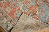 Distressed vintage Oushak rug corner displays brick red and mint green pile over woven foundation.