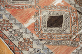 Distressed Oushak rug medallion featuring hook and latch motif, faded red, and dark brown.