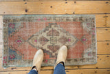 Distressed vintage Oushak rug mat, showcasing pale terracotta, blue, pink geometric design underfoot.