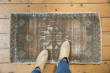 Distressed Oushak rug mat, revealing worn texture, exposed foundation, bronze and green tones.