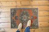 Distressed Oushak rug corner with terra cotta field, charcoal, and mint green medallion motifs.