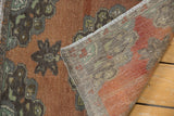 Curled vintage Oushak rug showing terracotta, charcoal, mint patterns, wear, and reverse.
