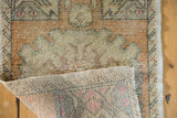 Distressed Oushak rug's corner with worn pile texture, faded orange border, and hand-knotted foundation.