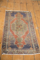 Distressed corner of a vintage Oushak rug, displaying blue, rust traditional patterns, and fringe.
