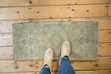Vintage distressed Oushak rug showing soft green and ivory playful floral patterns.