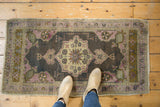 Distressed Oushak rug runner with charcoal, mauve, ivory floral medallion and feet.
