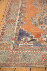 Distressed Oushak rug corner with abrashed terra cotta field and geometric blue border.