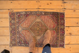 Distressed vintage Oushak rug mat with geometric medallion, faded aubergine, ivory, and mauve tones.