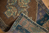 Vintage distressed Oushak rug pile with worn chocolate brown and blue geometric patterns.