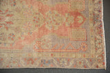 Distressed Oushak rug corner showing blush, antique ivory, silver hues, visible wear, and fringe.