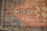 Distressed vintage Oushak rug corner, revealing geometric pattern and dusty mauve, slate silver tones.