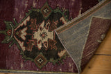 Folded corner of a vintage distressed Oushak rug, revealing worn aubergine pile and woven foundation.
