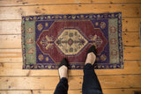 Distressed Oushak rug with aubergine field, violet borders, and ivory checker medallion.