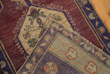 Folded vintage distressed Oushak rug showing aubergine field and sea foam green geometric border.