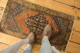 Corner of distressed Oushak rug with tangerine, gold, charcoal geometric patterns, showing even wear.