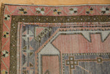 Distressed Oushak rug corner showing geometric patterns in blush, denim blue, and bronze.